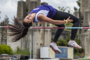 Athlete prepares for pole vault on a track with others watching.