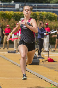 Athlete prepares for pole vault on a track with others watching.