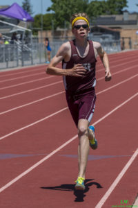 Athlete prepares for pole vault on a track with others watching.