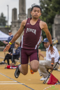 Athlete prepares for pole vault on a track with others watching.