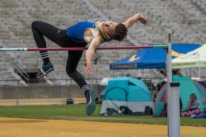 Athlete prepares for pole vault on a track with others watching.