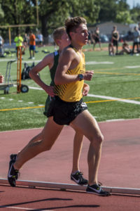 Athlete prepares for pole vault on a track with others watching.