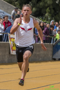 Athlete prepares for pole vault on a track with others watching.