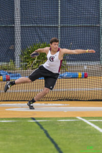 Athlete prepares for pole vault on a track with others watching.