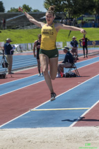Athlete prepares for pole vault on a track with others watching.