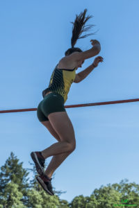 Athlete prepares for pole vault on a track with others watching.