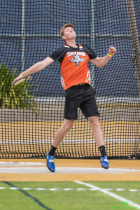 Athlete prepares for pole vault on a track with others watching.