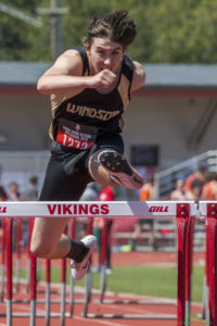 Athlete prepares for pole vault on a track with others watching.