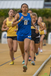 Athlete prepares for pole vault on a track with others watching.