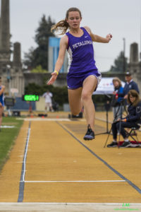 Athlete prepares for pole vault on a track with others watching.