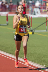 Athlete prepares for pole vault on a track with others watching.
