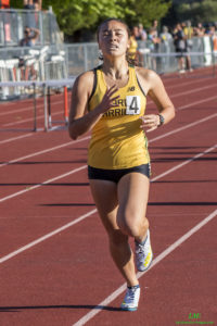 Athlete prepares for pole vault on a track with others watching.