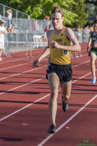 Athlete prepares for pole vault on a track with others watching.