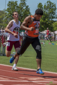 Athlete prepares for pole vault on a track with others watching.