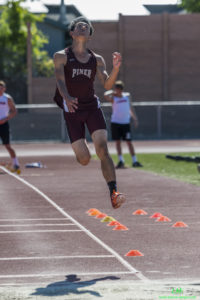 Athlete prepares for pole vault on a track with others watching.