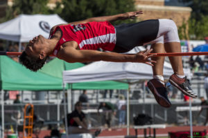 Athlete prepares for pole vault on a track with others watching.
