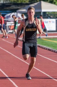 Athlete prepares for pole vault on a track with others watching.