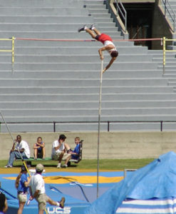 Athlete prepares for pole vault on a track with others watching.