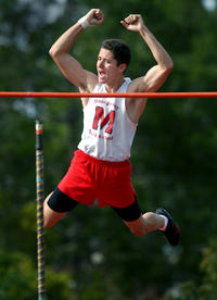 Athlete prepares for pole vault on a track with others watching.