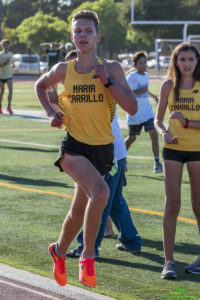 Athlete prepares for pole vault on a track with others watching.