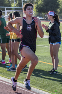 Athlete prepares for pole vault on a track with others watching.