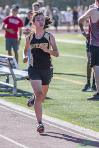 Athlete prepares for pole vault on a track with others watching.
