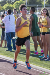 Athlete prepares for pole vault on a track with others watching.