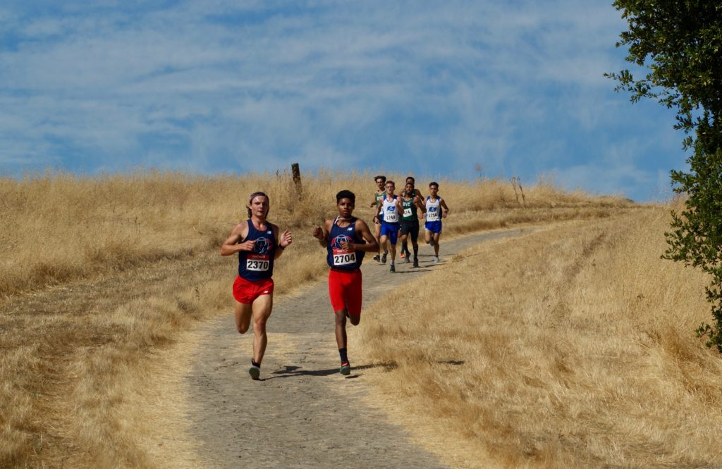 Athlete prepares for pole vault on a track with others watching.