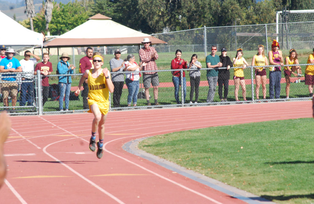 Athlete prepares for pole vault on a track with others watching.