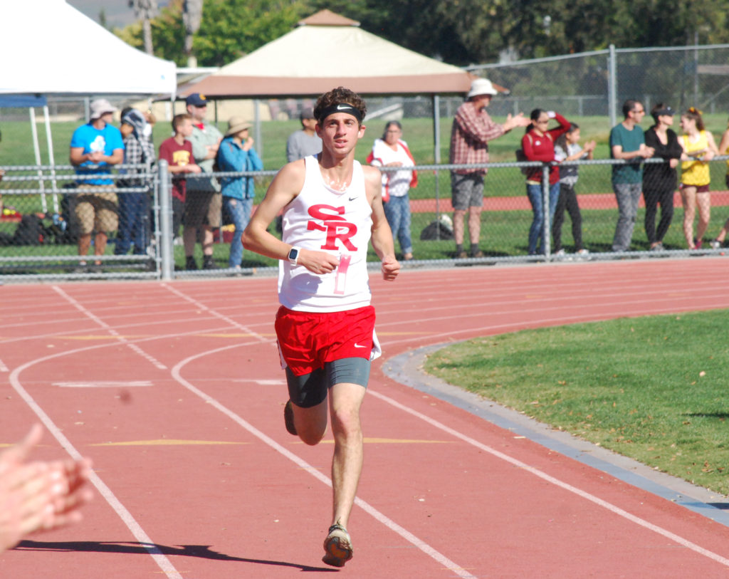 Athlete prepares for pole vault on a track with others watching.