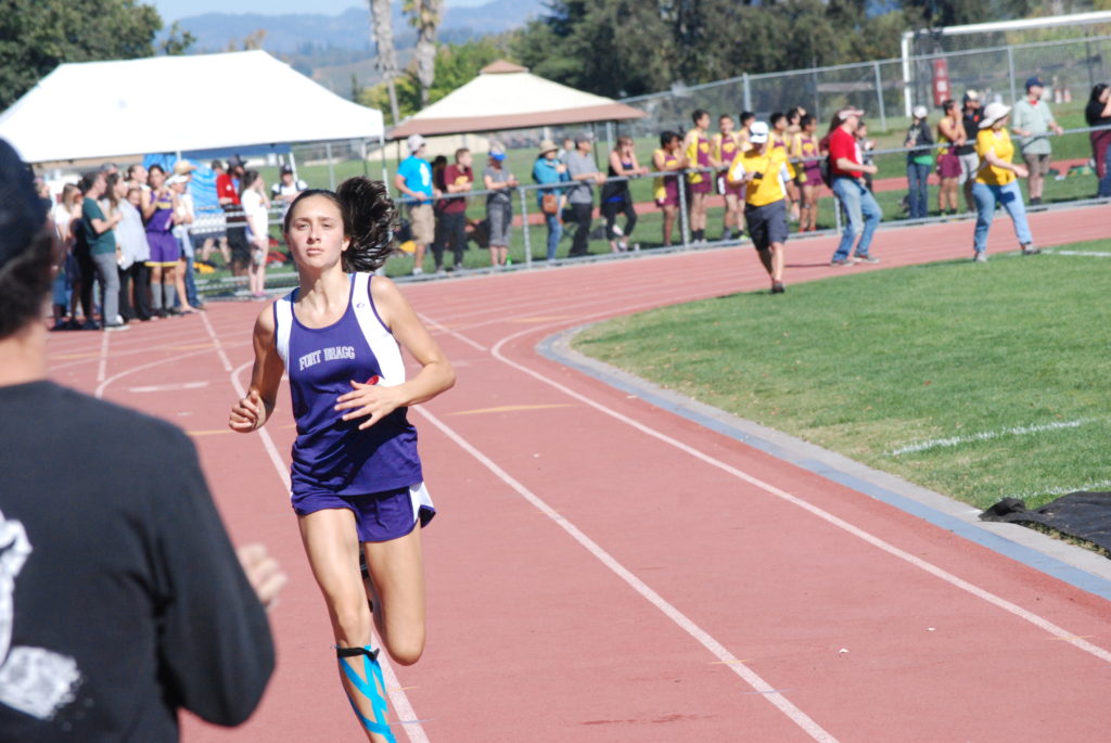 Athlete prepares for pole vault on a track with others watching.