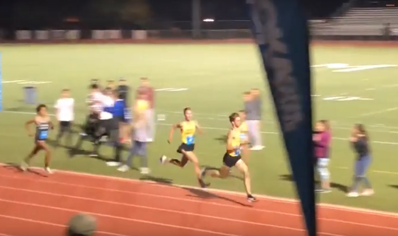 Athlete prepares for pole vault on a track with others watching.