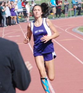 Athlete prepares for pole vault on a track with others watching.