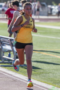 Athlete prepares for pole vault on a track with others watching.
