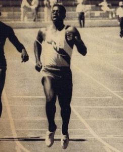 Athlete prepares for pole vault on a track with others watching.