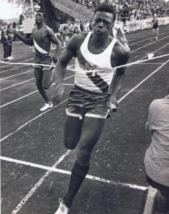 Athlete prepares for pole vault on a track with others watching.