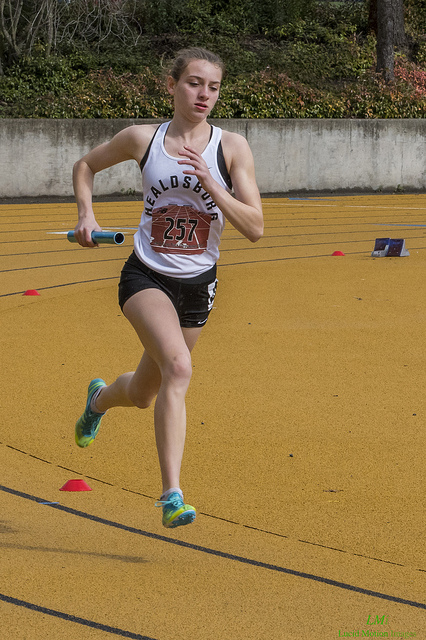 Athlete prepares for pole vault on a track with others watching.