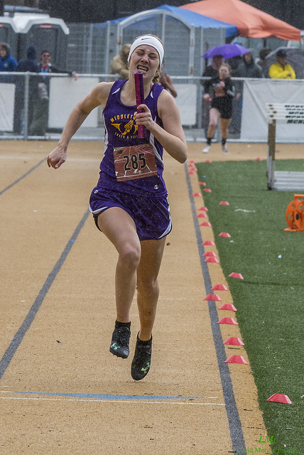 Athlete prepares for pole vault on a track with others watching.