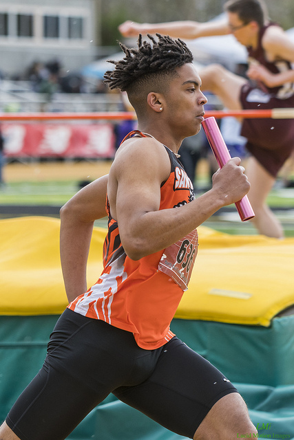 Athlete prepares for pole vault on a track with others watching.