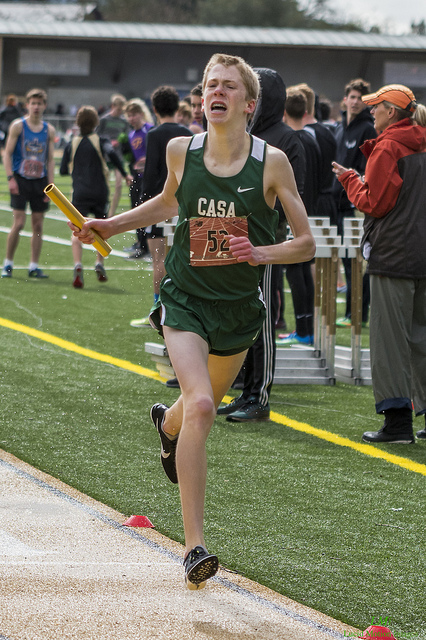 Athlete prepares for pole vault on a track with others watching.