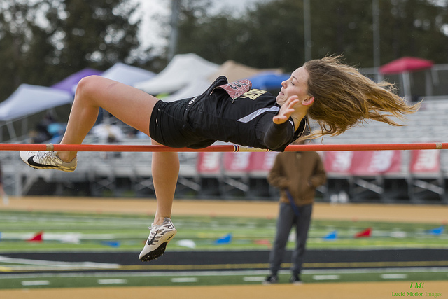 Athlete prepares for pole vault on a track with others watching.