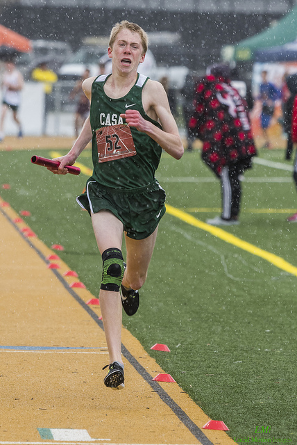 Athlete prepares for pole vault on a track with others watching.