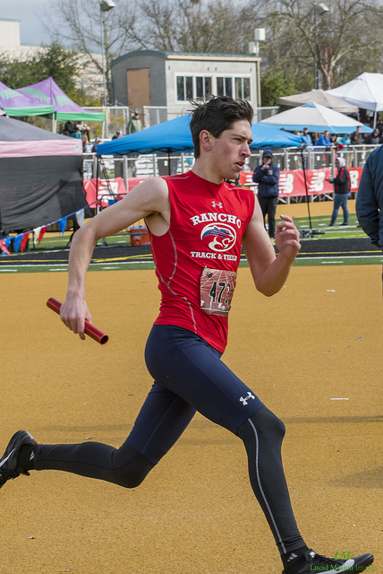 Athlete prepares for pole vault on a track with others watching.