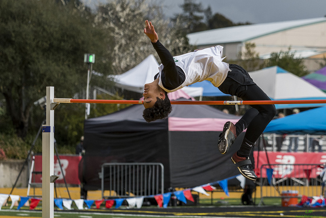 Athlete prepares for pole vault on a track with others watching.