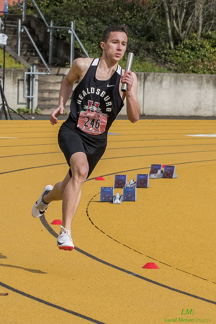 Athlete prepares for pole vault on a track with others watching.