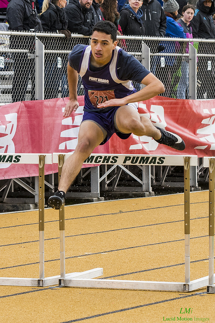 Athlete prepares for pole vault on a track with others watching.