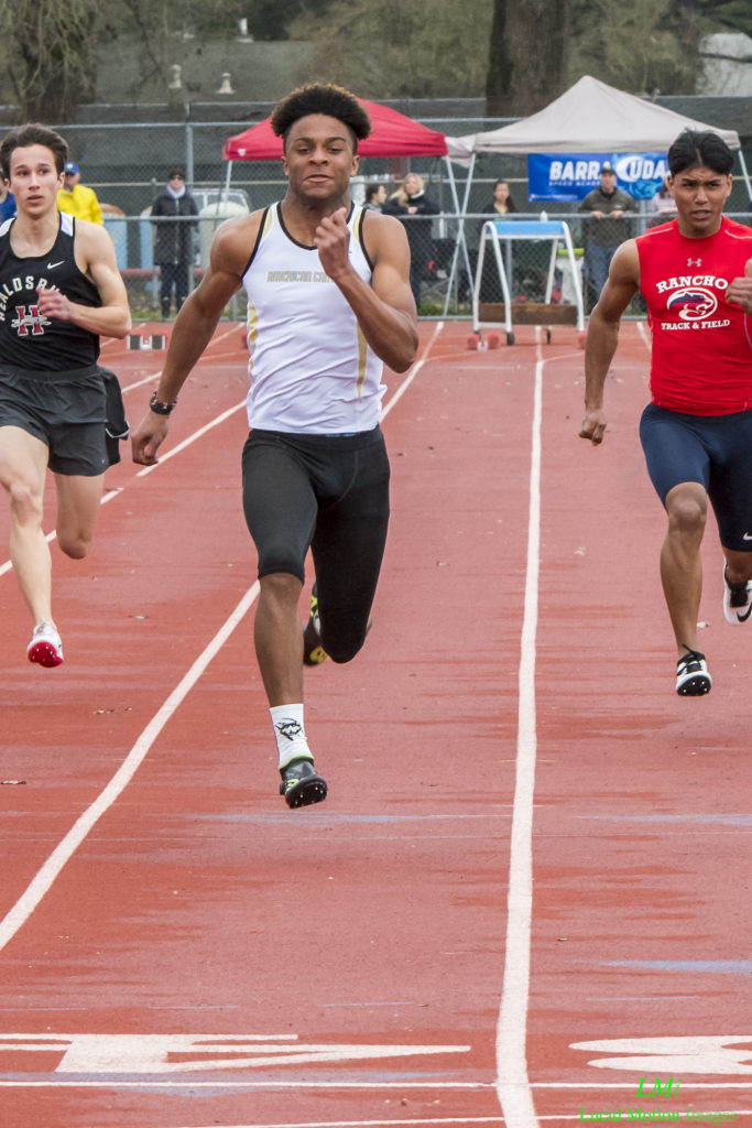 Athlete prepares for pole vault on a track with others watching.