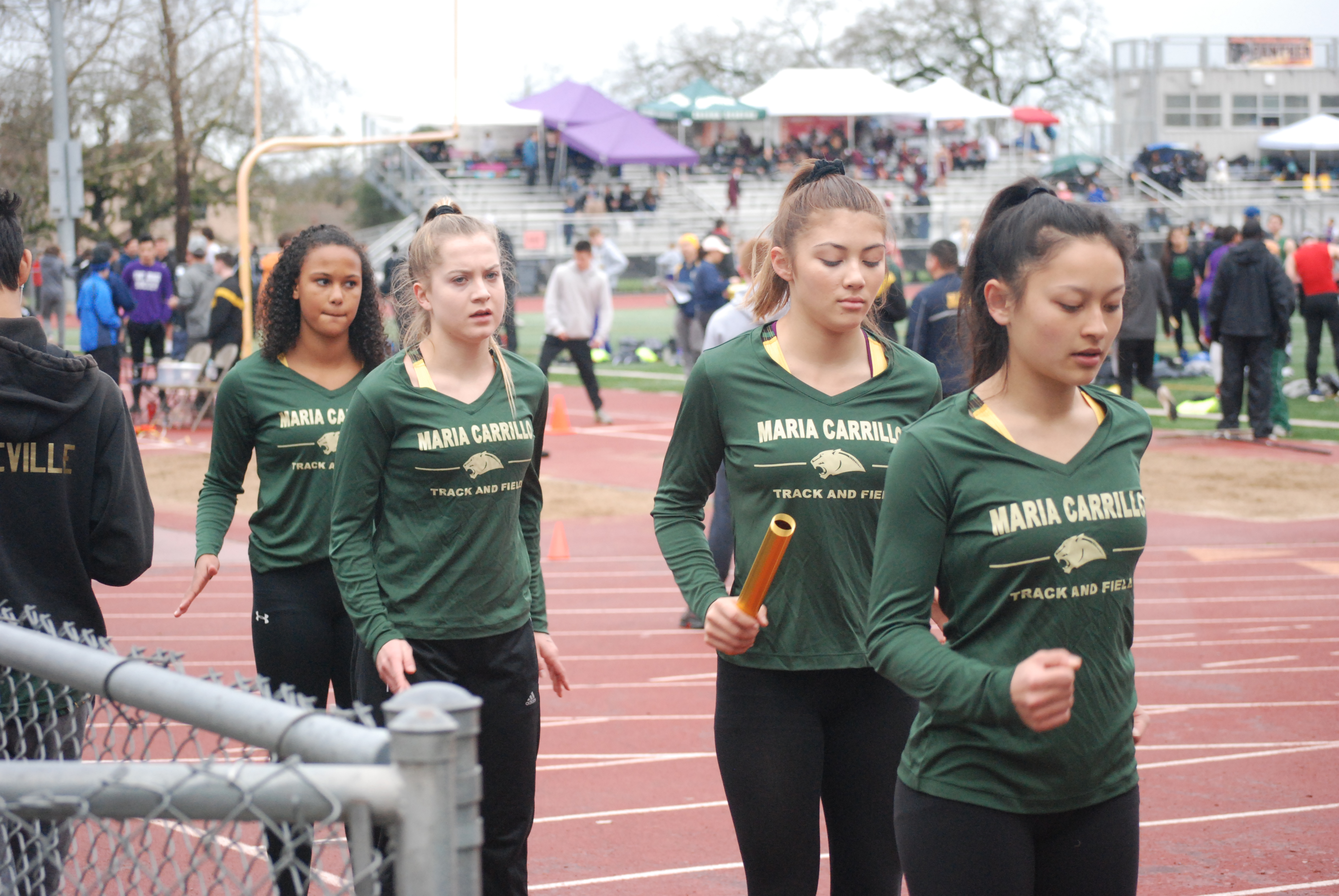 Athlete prepares for pole vault on a track with others watching.