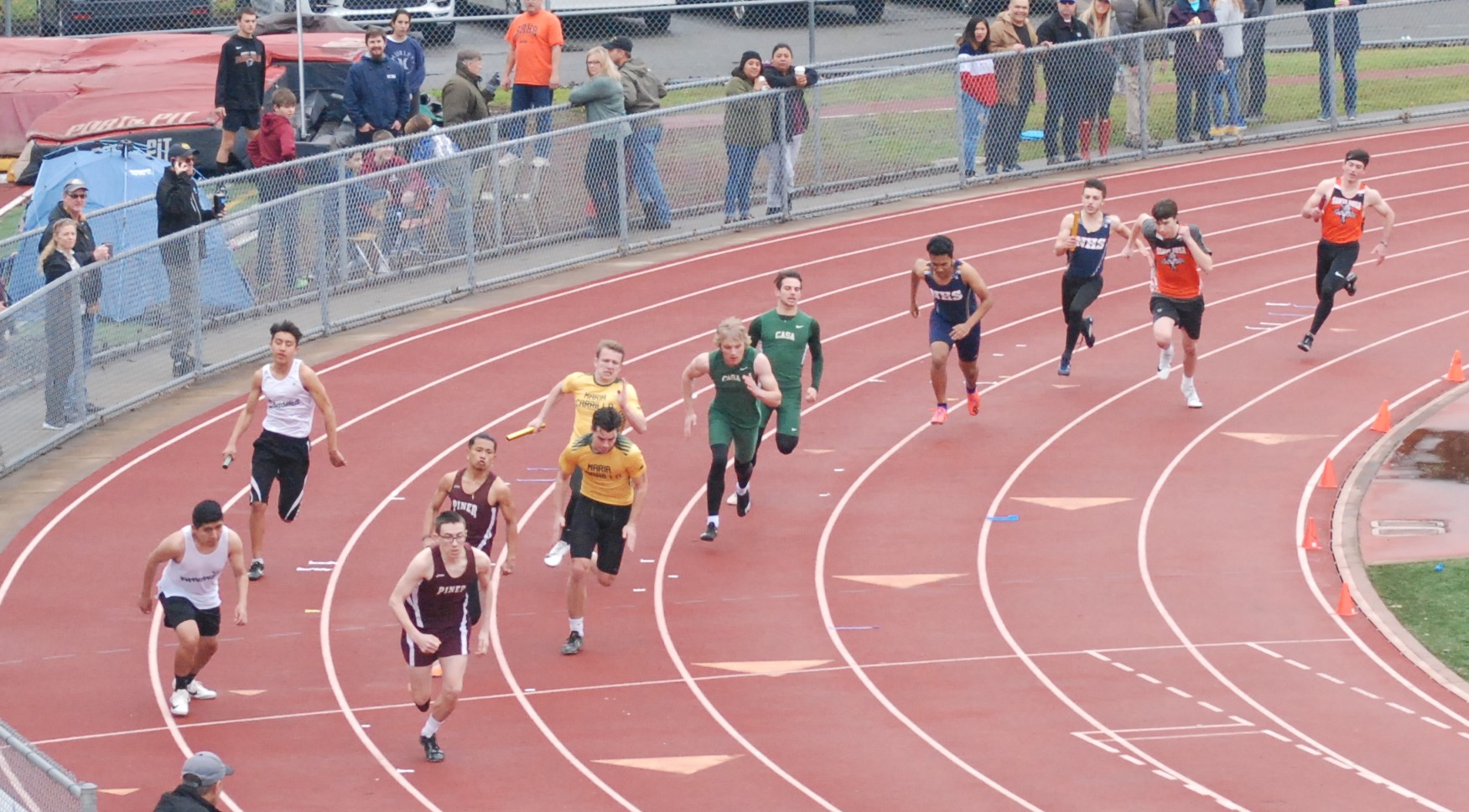 Athlete prepares for pole vault on a track with others watching.
