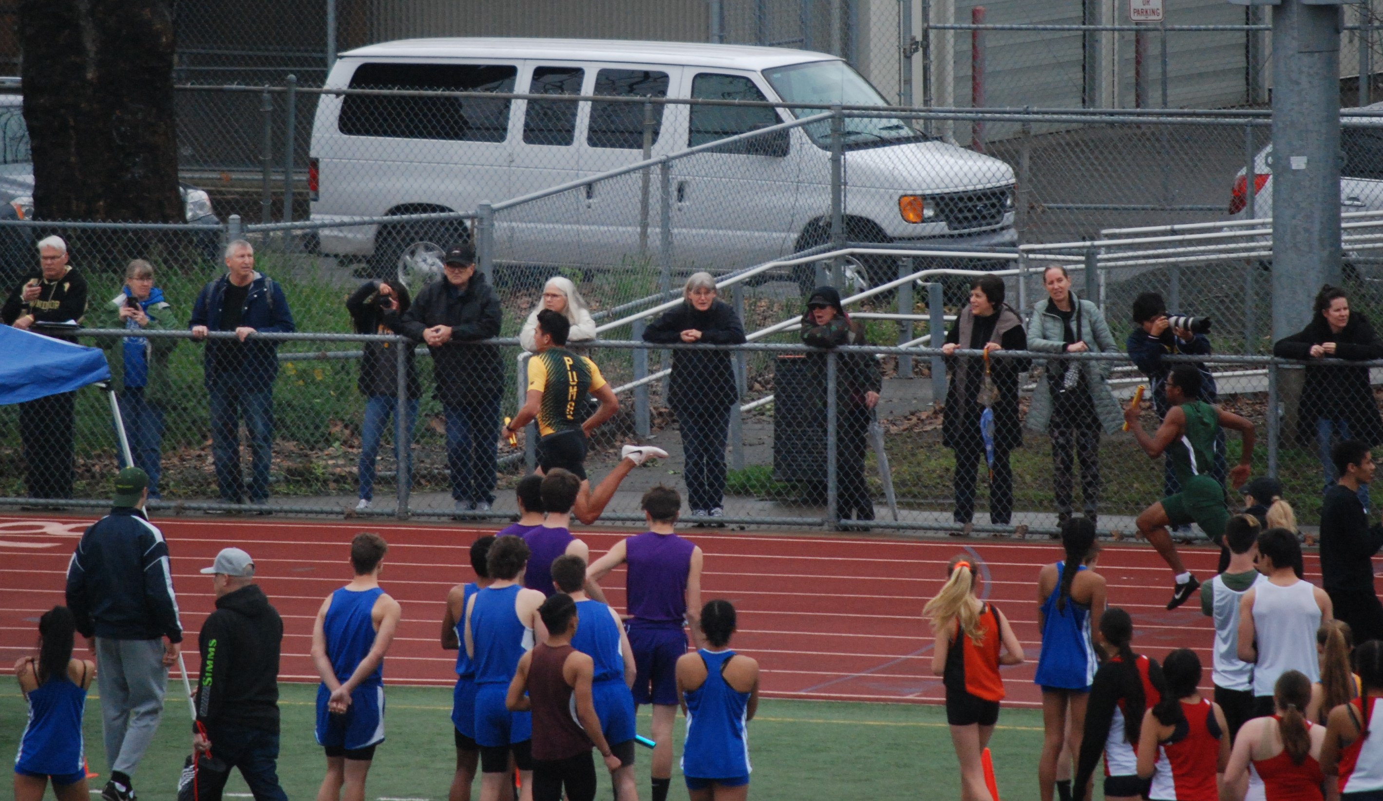 Athlete prepares for pole vault on a track with others watching.